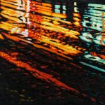 A rainy night in a rural town in Ontario: green, yellow and red light reflections of a Shell station shine on the wavy wet road